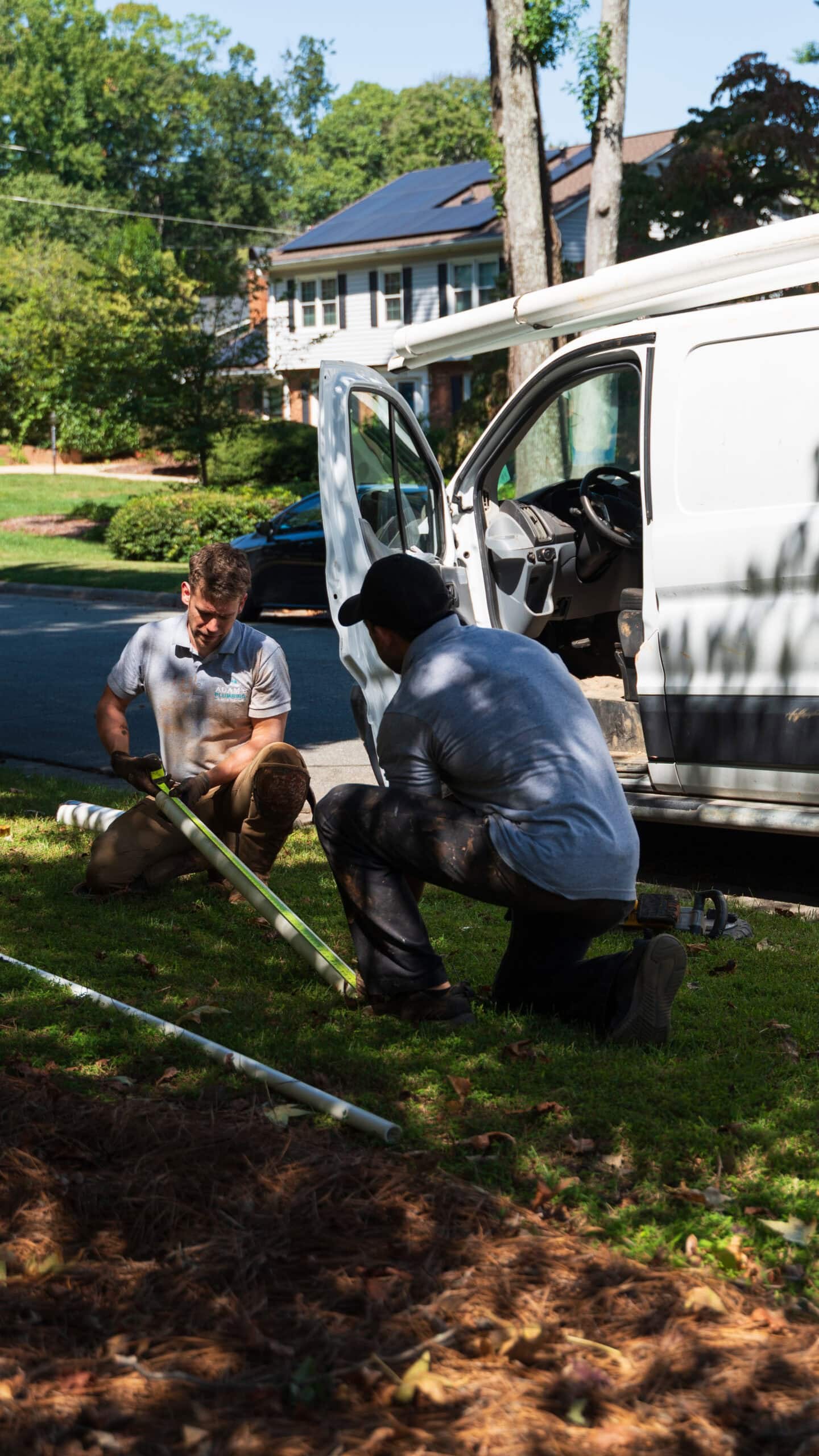 Two plumbers from the crew working outside a customer's home beside the van